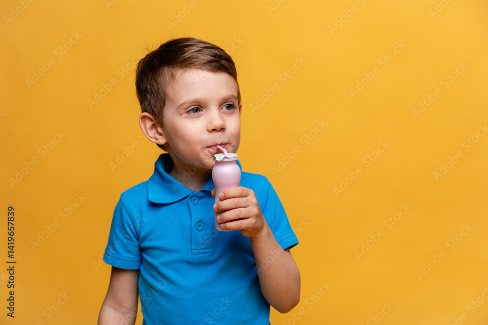 Cute little brunette girl in blue t-shirt drinking tasty yogurt from a plastic bottle on light yellow background. Healthy nutrition concept. Copy space. High quality photo
