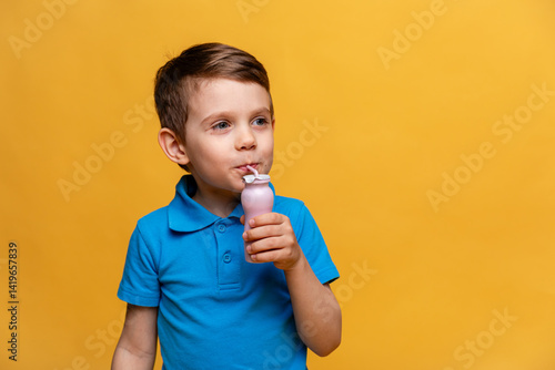 Obraz na płótnie Cute little brunette girl in blue t-shirt drinking tasty yogurt from a plastic bottle on light yellow background. Healthy nutrition concept. Copy space. High quality photo w salonie