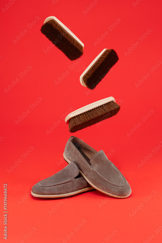 New of suede loafers pair of boots with flying shoe brushes on a orange background. New of suede loafers pair of boots with flying shoe brushes on a orange background.