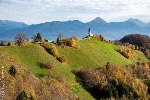 Obraz na płótnie Jamnik church standing on a hill with autumn foliage and mountains in the background w salonie
