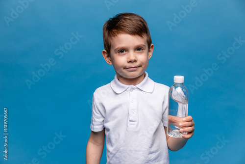 A happy little boy drinks water for health on a blue background. The child is holding a water bottle. A kid with a plastic bottle. Children's activity and energy, generation Z. body hydration concept