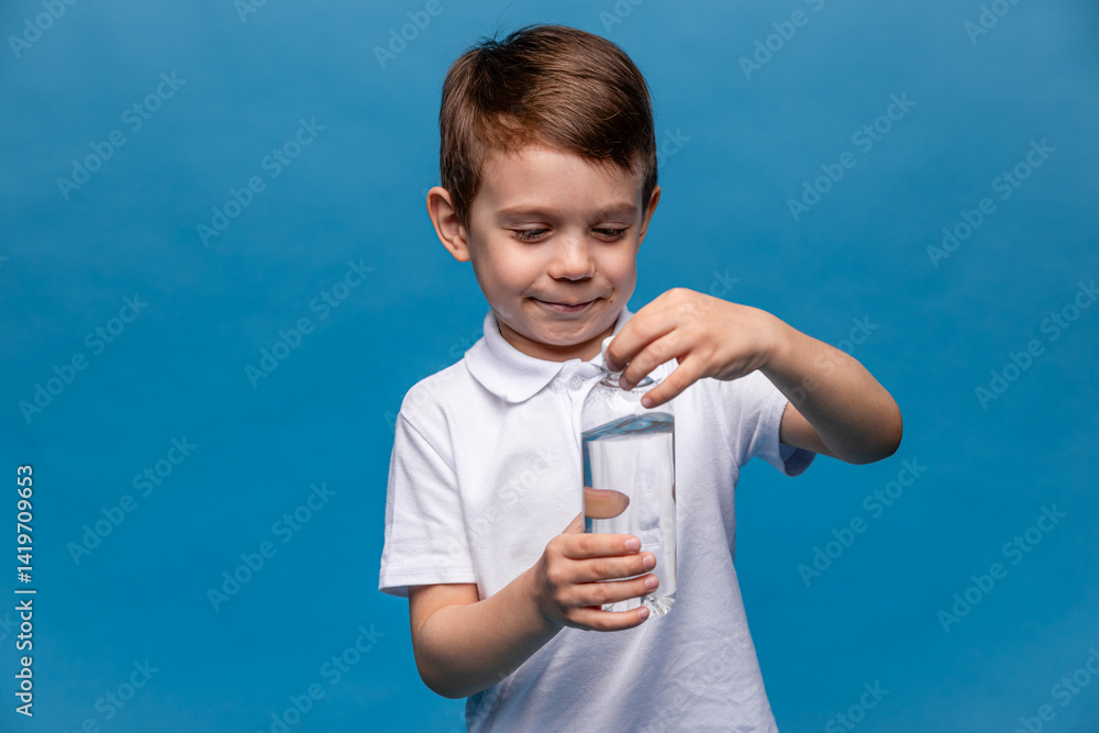 Happy little boy drinks water for health on a blue background. The child is opening a bottle of water. A kid with a plastic bottle. Children's activity and energy, generation Z. body hydration concept