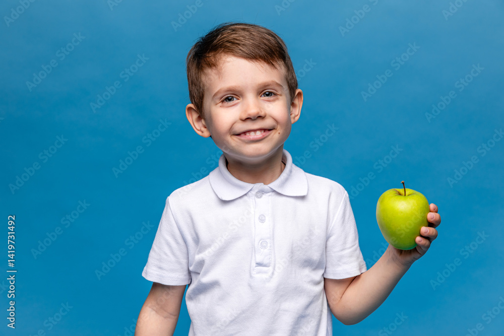 Happy little boy in white t-shirt holding green apple isolated on blue background. Proper nutrition. Child health. vegetarianism. High quality photo. Copy space