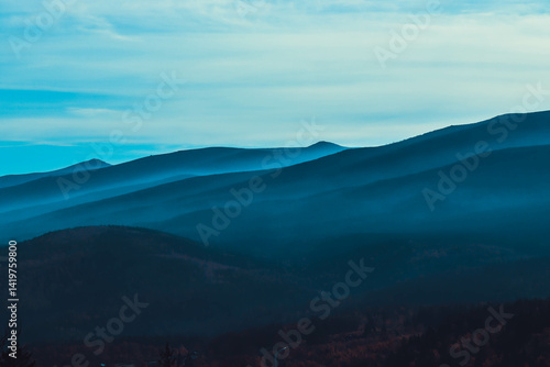 Mountain Serenity: A panoramic view of majestic mountain ranges fading into the distance, veiled in a cool, ethereal mist beneath a tranquil sky, evoking feelings of peace and solitude.