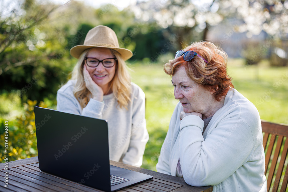 Fototapeta premium Happy moment of smiling woman with her senior mother while watching laptop screen in garden