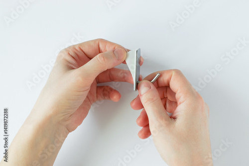 Self-adhesive metal chrome hook on the wall in the hands of a Caucasian woman. Tears off the sticky layer.