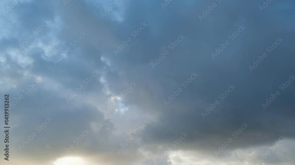 Timelapse of dramatic sunbeams shining through large dark storm clouds overhead for abstract natural backgrounds