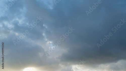 Timelapse of dramatic sunbeams shining through large dark storm clouds overhead for abstract natural backgrounds