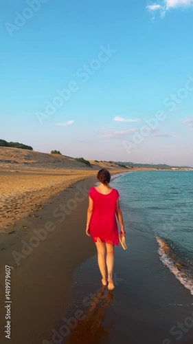 beautiful woman in a red dress walking down the beach while the waves splash her feet