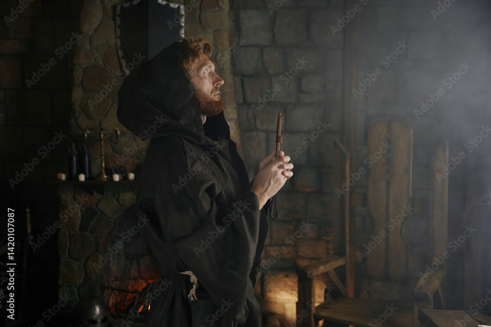 Faithful priest in robe hood praying with rosary beads and cross