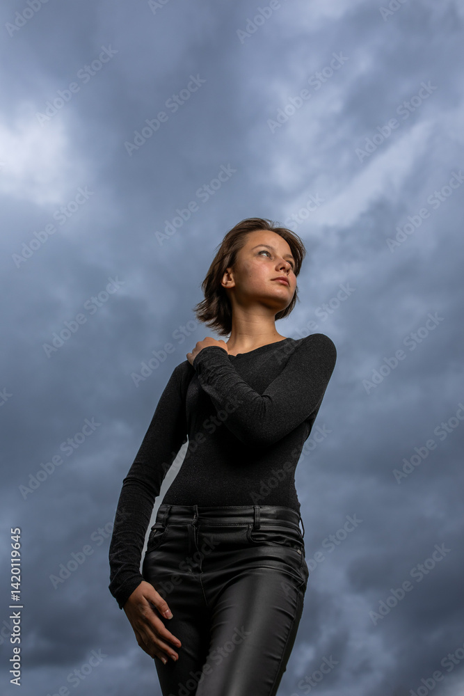 Portrait of beautiful serious teen girl with closed eyes against cloudy sky on windy day.