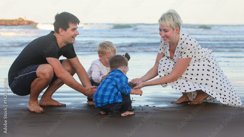 Fototapeta premium portrait of cheerful young couple with two little boys on the beach at dusk by the ocean bonding