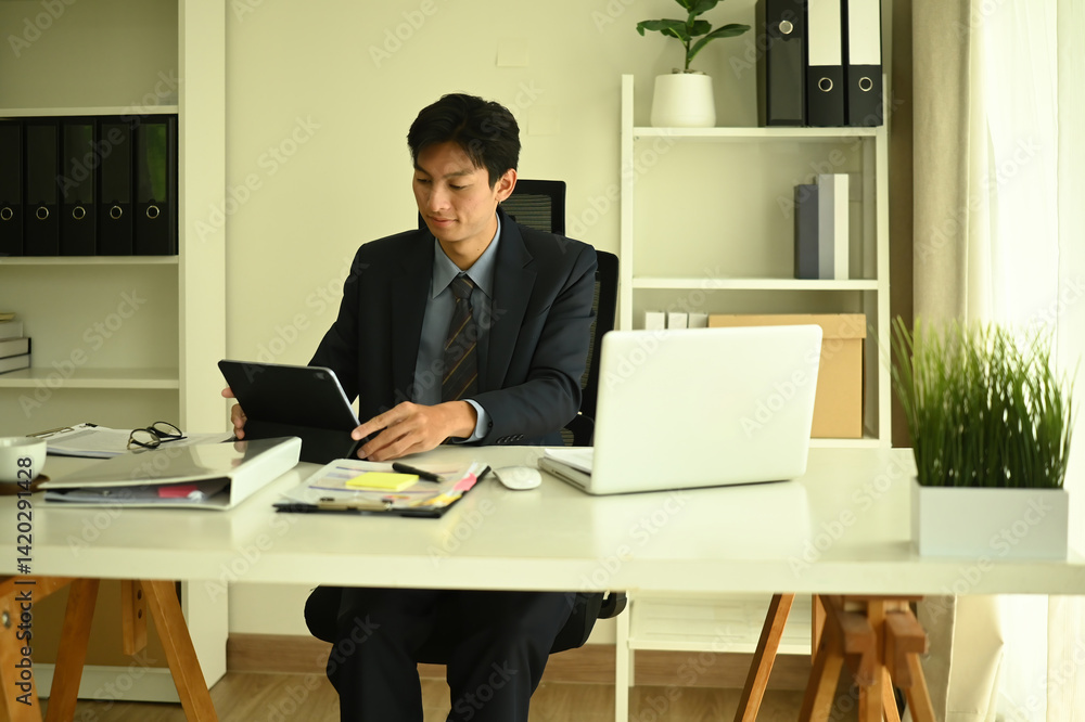 Confident Executive Working with Tablet and Laptop at Desk Confident Executive Working with Tablet and Laptop at Desk