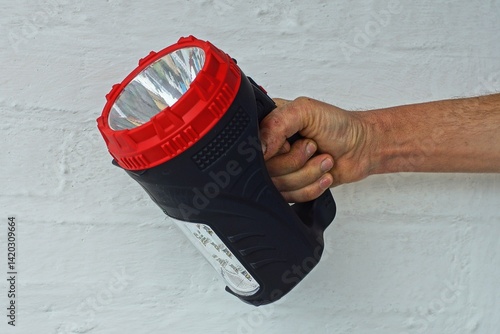 one powerful new round plastic off with white reflector battery operated electric with handle big black flashlight in hand of man near wall of house