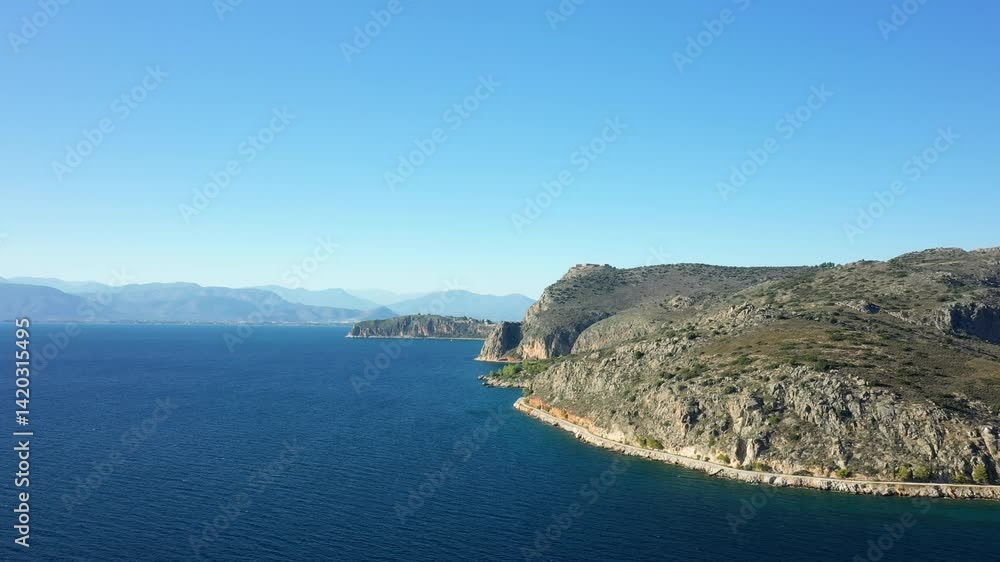 The barren rocky coastline bordered by green countryside and coves, in Europe, Greece, Peloponnese, Argolis, Nafplio, on the Myrtos Sea, in summer, on a sunny day. The barren rocky coastline bordered by green countryside and coves, in Europe, Greece, Peloponnese, Argolis, Nafplio, on the Myrtos Sea, in summer, on a sunny day.