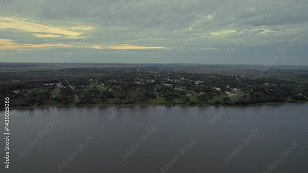 view of tranquil lake with a village and lush greenery on the lakeshore under overcast sunset sky view of tranquil lake with a village and lush greenery on the lakeshore under overcast sunset sky