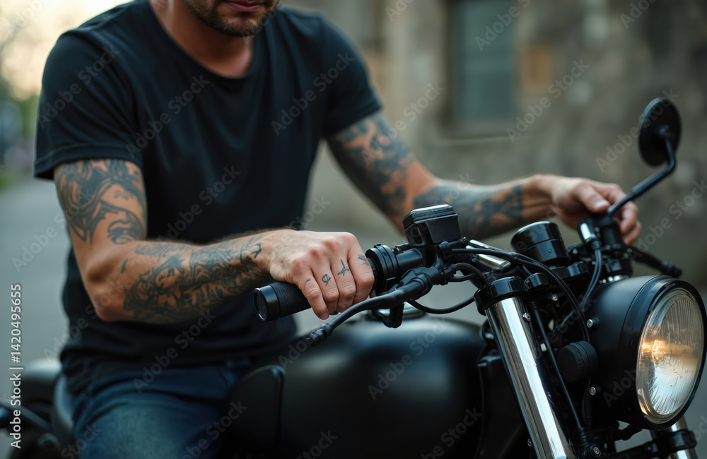 Man in black t-shirt sits on black motorbike. Biker has tattoos on arms holding handles. Urban lifestyle concept, fashion. Closeup of tattooed arms and black motorcycle details.