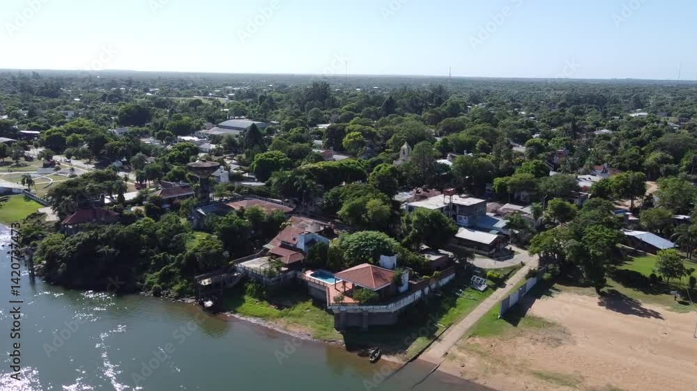 Drone view from the river showing the weekend homes and vegetation along the coast of Paso de la Patria. The sun's reflection on the water and the proximity to the waterfront avenue are observed Drone view from the river showing the weekend homes and vegetation along the coast of Paso de la Patria. The sun's reflection on the water and the proximity to the waterfront avenue are observed