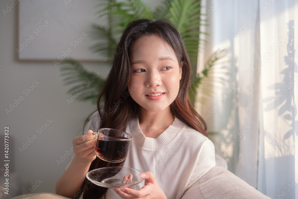 Smiling young woman holding a clear glass cup of coffee and looking out of window. Smiling young woman holding a clear glass cup of coffee and looking out of window.