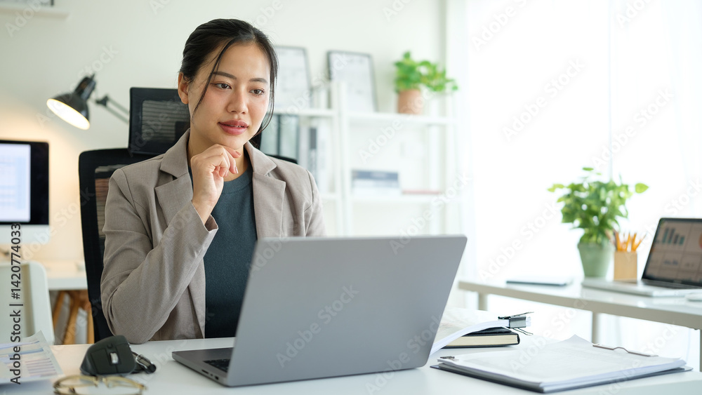 Professional businesswoman in a stylish blazer analyzing work on her laptop at modern office. Professional businesswoman in a stylish blazer analyzing work on her laptop at modern office.