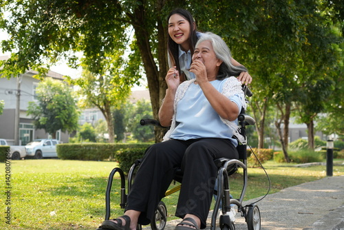 Two women, the daughter pushing a stroller with her elderly mother, walk in the garden and chat happily.