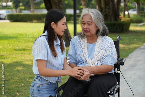 Two women, the daughter pushing a stroller with her elderly mother, walk in the garden and chat happily.
