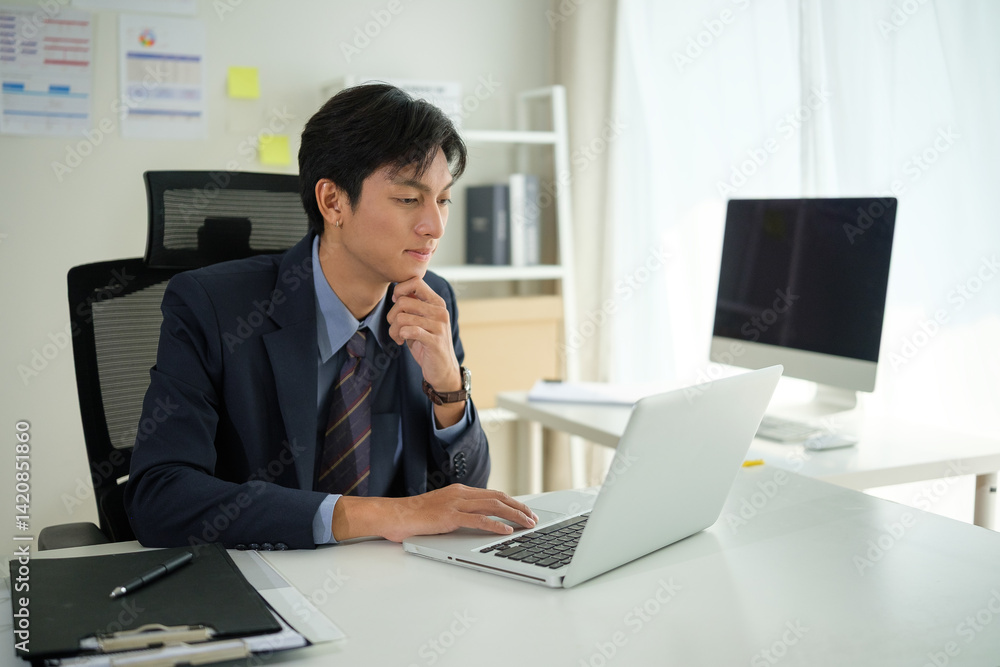 Businessman sitting at a desk with thoughtful expression while reviewing information on his laptop. Businessman sitting at a desk with thoughtful expression while reviewing information on his laptop.