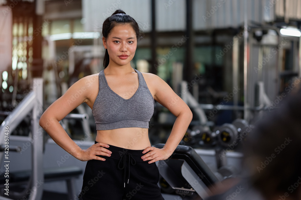 Obraz premium Confident athletic female standing with hands on hips in gym, showing strength and commitment to fitness goals.