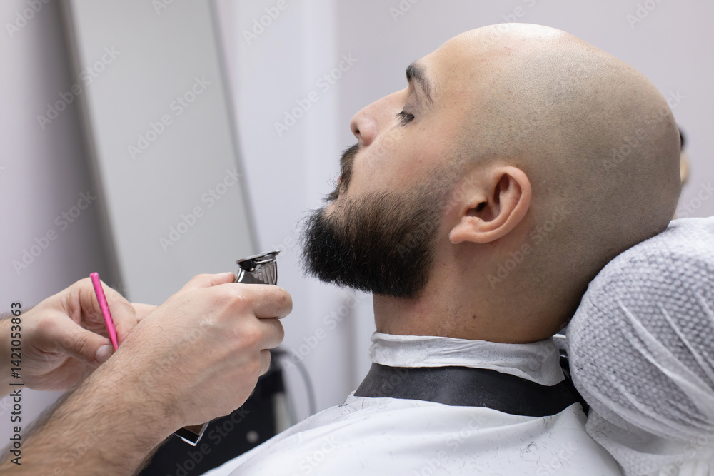 Bald man is getting his beard trimmed by barber. The bald man is laying down on a chair while the other man is holding a pair of scissors and trimming his beard Bald man is getting his beard trimmed by barber. The bald man is laying down on a chair while the other man is holding a pair of scissors and trimming his beard