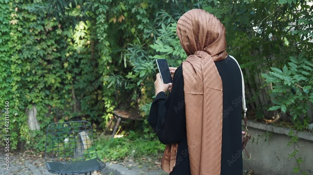 Woman in hijab using smartphone in lush garden setting Woman in hijab using smartphone in lush garden setting