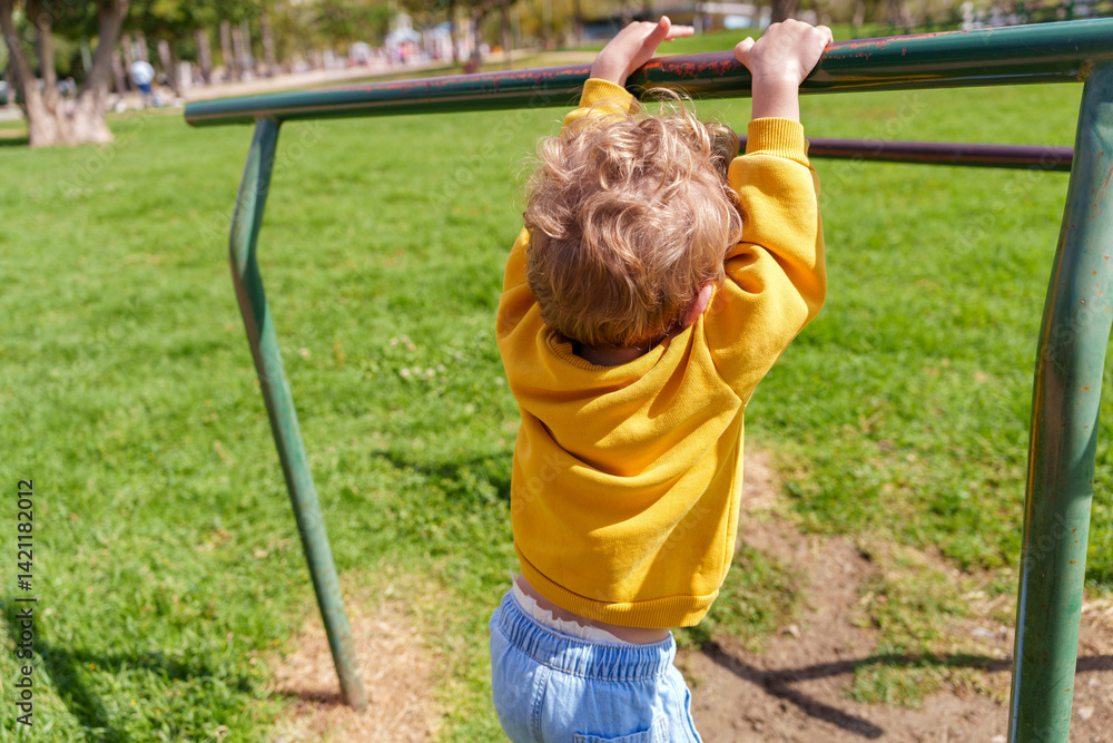 Little child with yellow sweatshirt having fun and training at playground by hanging from horizontal bar Little child with yellow sweatshirt having fun and training at playground by hanging from horizontal bar