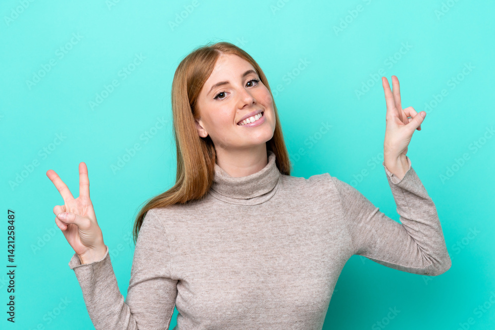 Young redhead woman isolated on blue background showing victory sign with both hands Young redhead woman isolated on blue background showing victory sign with both hands