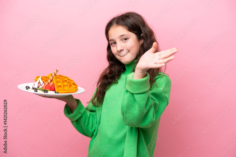 Little caucasian girl holding waffles isolated on pink background saluting with hand with happy expression Little caucasian girl holding waffles isolated on pink background saluting with hand with happy expression