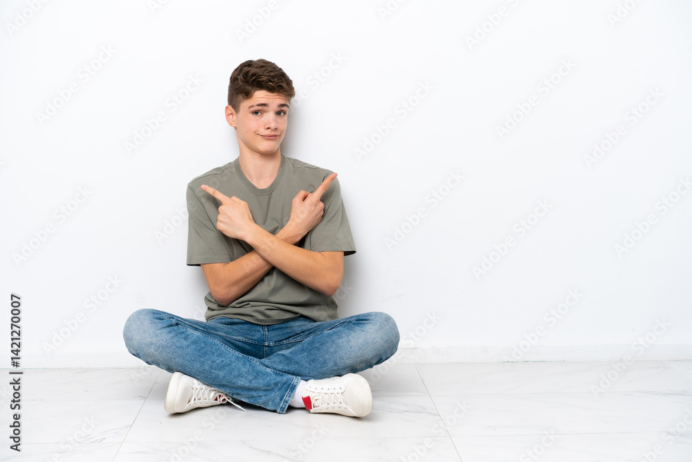 Teenager Russian man sitting on the floor isolated on white background pointing to the laterals having doubts Teenager Russian man sitting on the floor isolated on white background pointing to the laterals having doubts