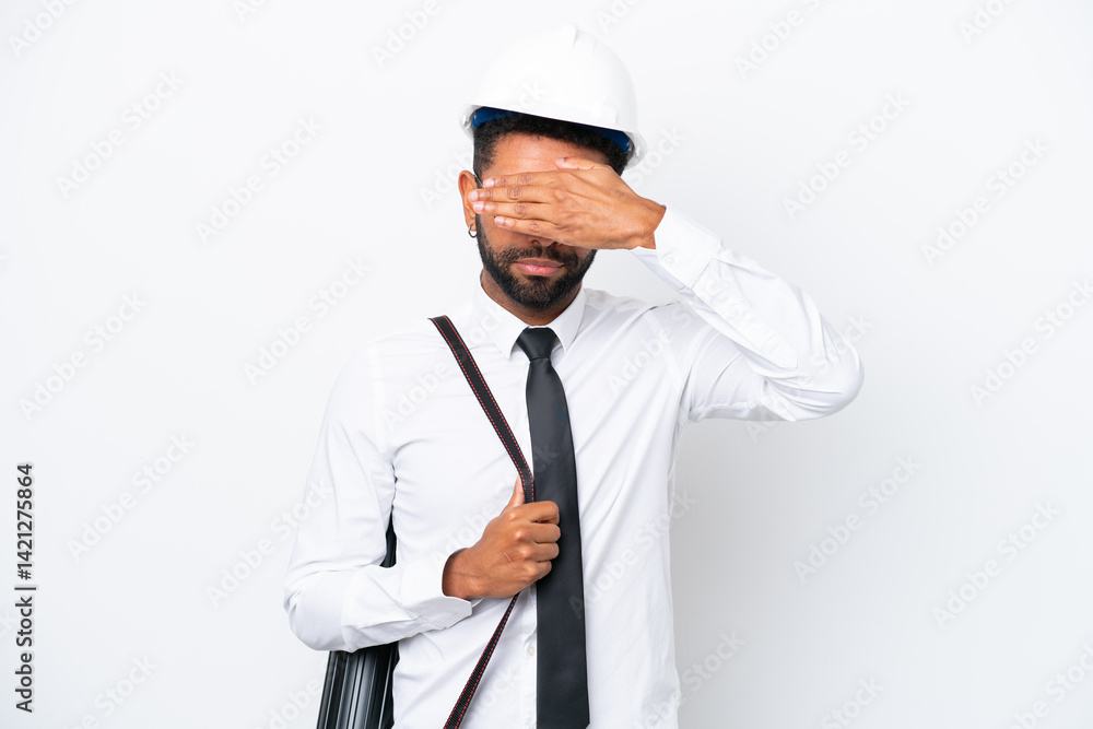 Young architect Brazilian man with helmet and holding blueprints isolated on white background covering eyes by hands. Do not want to see something Young architect Brazilian man with helmet and holding blueprints isolated on white background covering eyes by hands. Do not want to see something