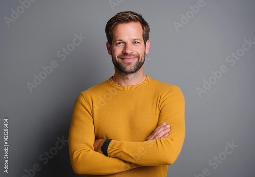 Confident smiling man in yellow sweater standing with arms crossed against grey background, casual stylish look, positive attitude portrait 