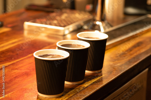 Three steaming takeaway cups of hot chocolate on a rustic wooden counter, lit by warm ambient lights, evoking cozy winter evenings.