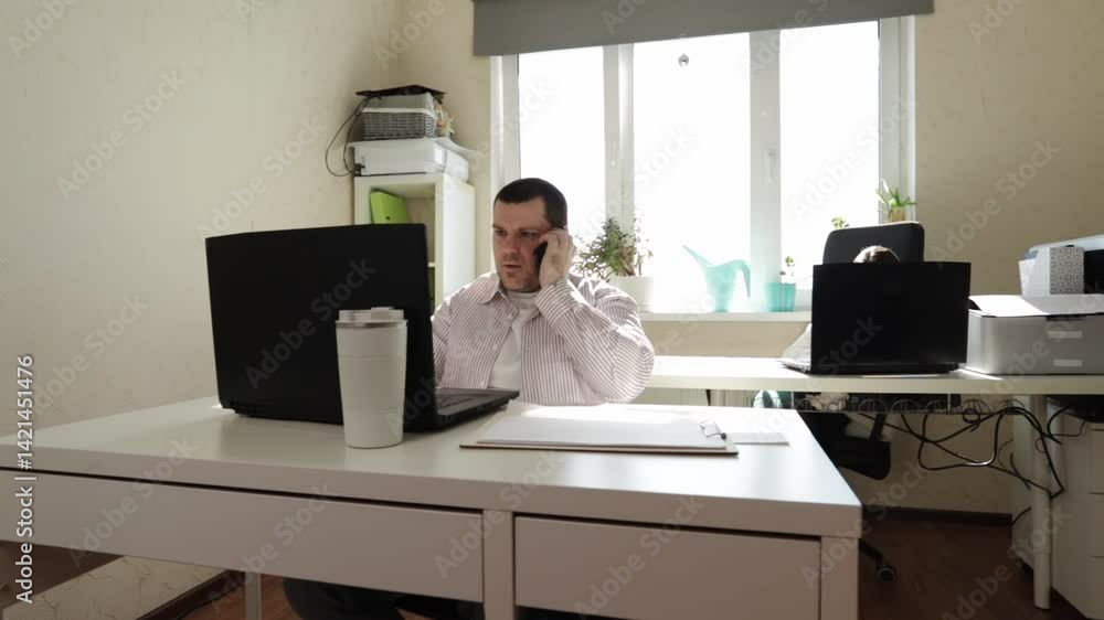 Professional Worker Engaged in Phone Conversation While Typing on Laptop at Desk Professional Worker Engaged in Phone Conversation While Typing on Laptop at Desk