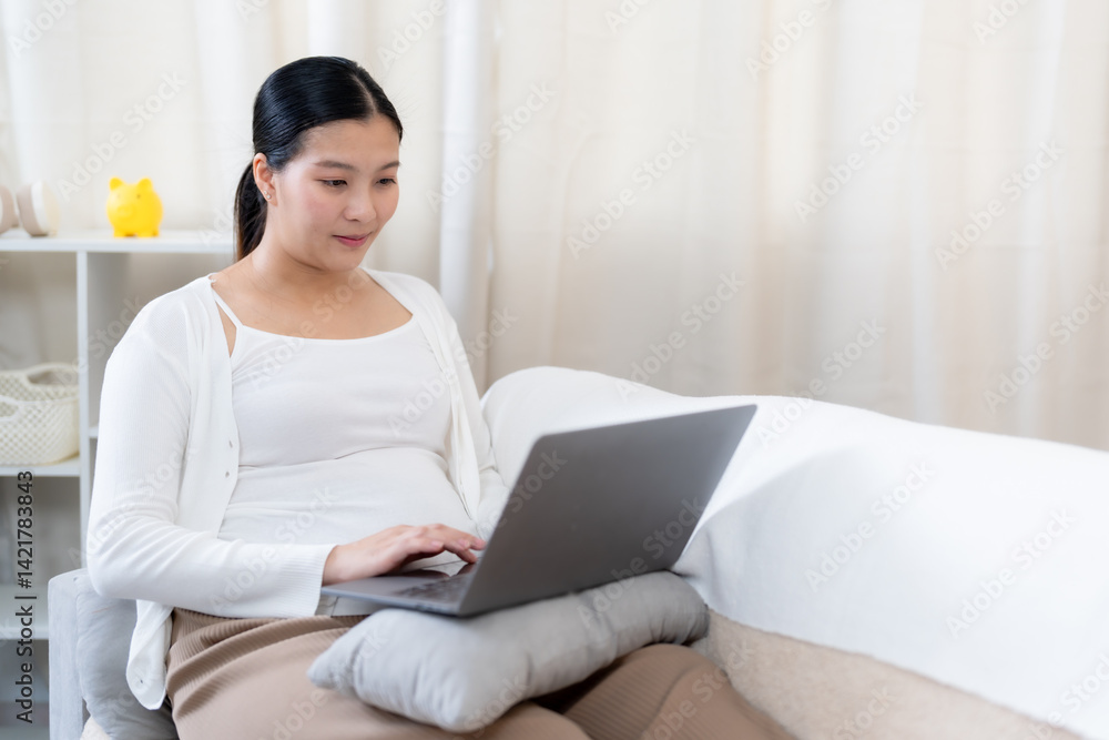 Asian pregnant adult woman sitting on sofa using laptop resting hands on keyboard wearing casual white clothes looking at screen with calm mood showing lifestyle balance technology prenatal care Asian pregnant adult woman sitting on sofa using laptop resting hands on keyboard wearing casual white clothes looking at screen with calm mood showing lifestyle balance technology prenatal care