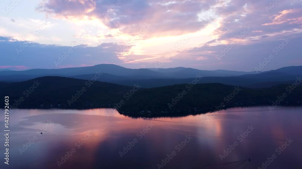 Aerial view of a peaceful lake at sunset with forested hills and distant mountains beneath a glowing, colorful sky. Maidstone Lake Vermont and the Green Mountains. Aerial view of a peaceful lake at sunset with forested hills and distant mountains beneath a glowing, colorful sky. Maidstone Lake Vermont and the Green Mountains.