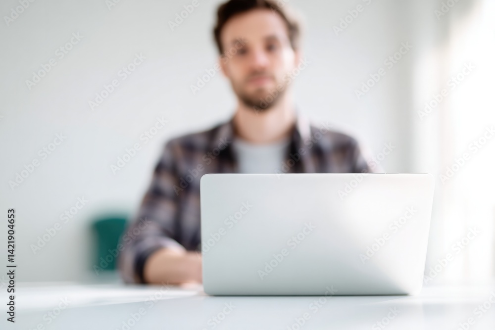 front-facing portrait of individual working remotely at desk with laptop background intentionally blurred to emphasize front-facing portrait of individual working remotely at desk with laptop background intentionally blurred to emphasize