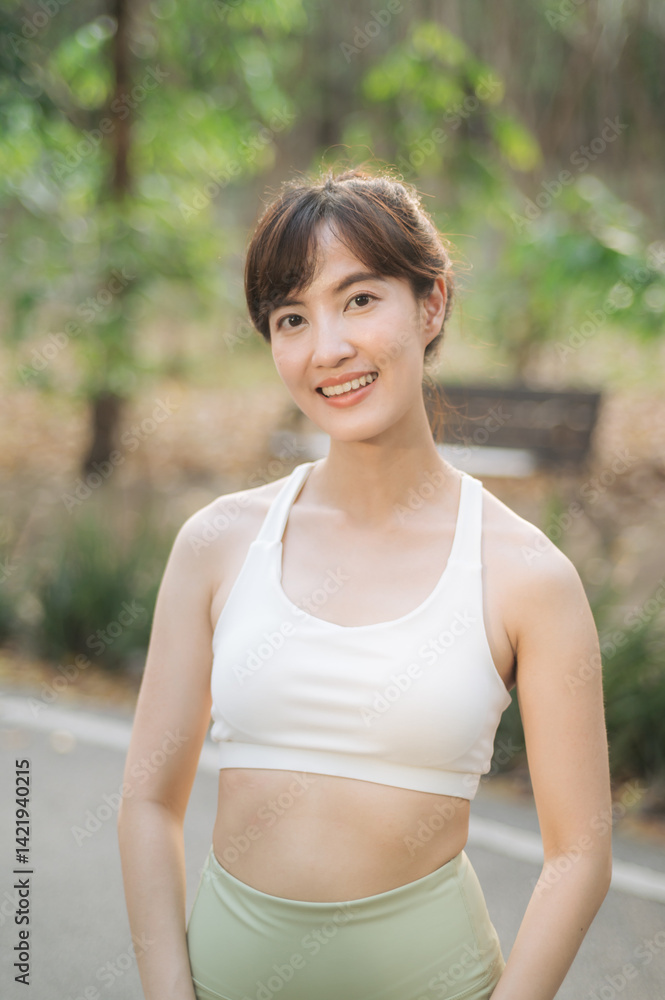 Fototapeta premium Asian woman outdoor workout. Healthy and active lifestyle concept. Smiling young woman in sportswear enjoying exercise in natural park