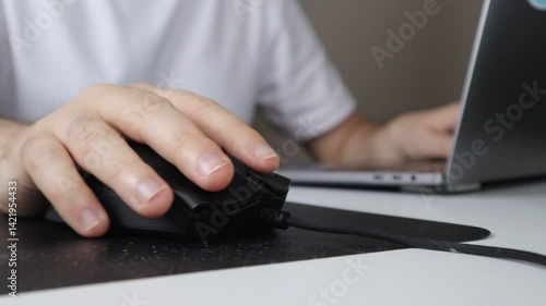Close-up of a hand using a computer mouse while working on a laptop at a desk