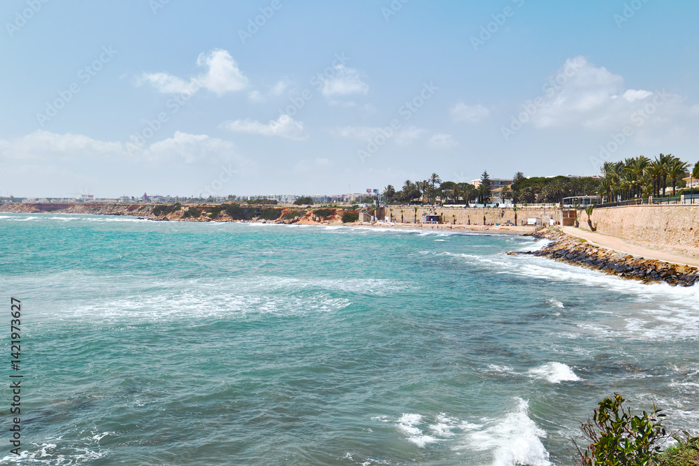 Fototapeta premium Scenic coastline of Punta Prima, turquoise waters of Mediterranean Sea, rocky cliffs along shoreline. Costa Blanca, Province of Alicante, Spain