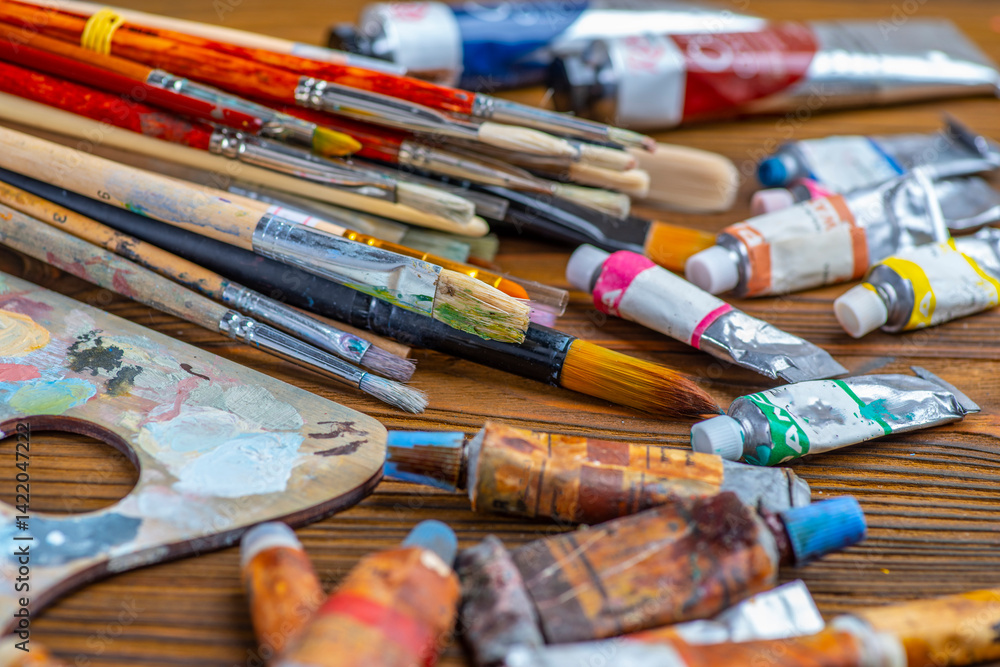 Obraz premium Old used brushes and paint tubes in an artist's studio, palette with multi-colored spots of oil or acrylic paint