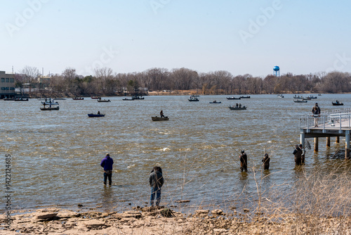 People fishing in boats and on the river shoreline on Fox river in Spring at De Pere, Wisconsin