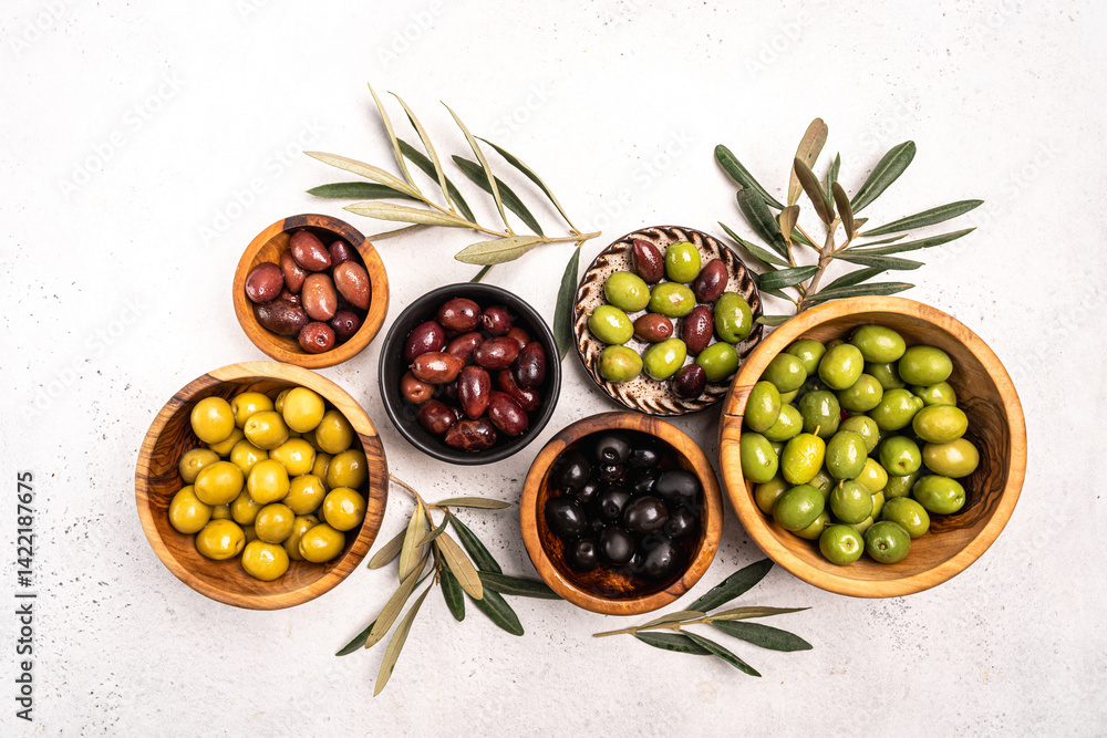 Green and black olives in a bowls and olive oil on white background top view. Olive oil and variety of green and black olives in bowls with olive leaves all around taken from above.
