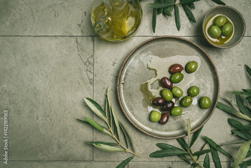 Obraz na płótnie Green and black olives in a bowls and olive oil on gray background top view. Olive oil and variety of green and black olives in bowls with olive leaves all around taken from above. w salonie