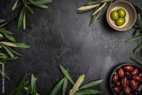 Obraz na płótnie Green and black olives in a bowls and olive oil on dark background top view. Olive oil and variety of green and black olives in bowls with olive leaves all around taken from above. w salonie