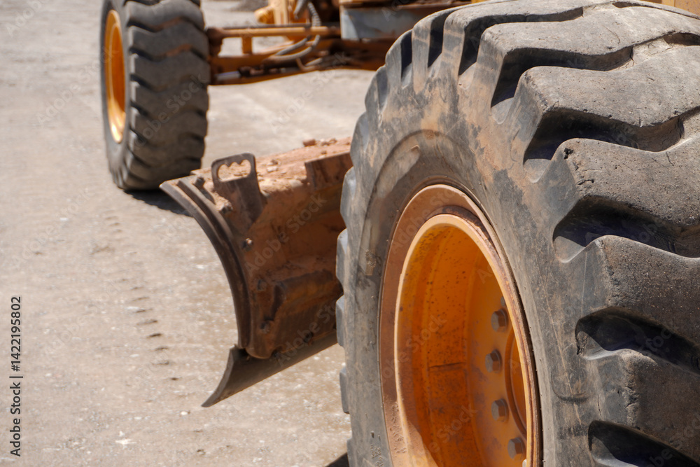 A close-up view of a large, rugged tire with deep treads, showcasing an orange rim. The background features a dusty surface, hinting at construction activity. A close-up view of a large, rugged tire with deep treads, showcasing an orange rim. The background features a dusty surface, hinting at construction activity.